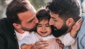 LGBTQ couple kissing their egg donor conceived daughter.