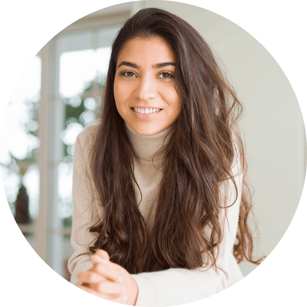 A woman wearing a taupe turtleneck is smiling and poses with her hands clasped leaning against a countertop.