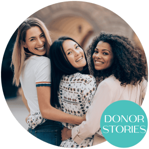A group of three women embrace each other and looks back smiling.