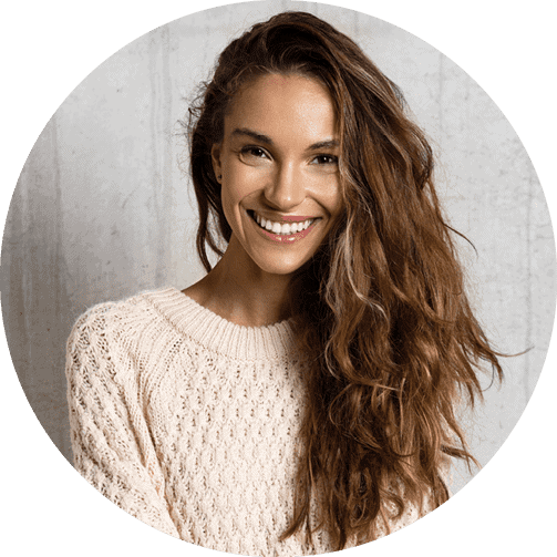 A woman in a cream cable-knit sweater with her long hair gathered on one side smiles confidently directly ahead.