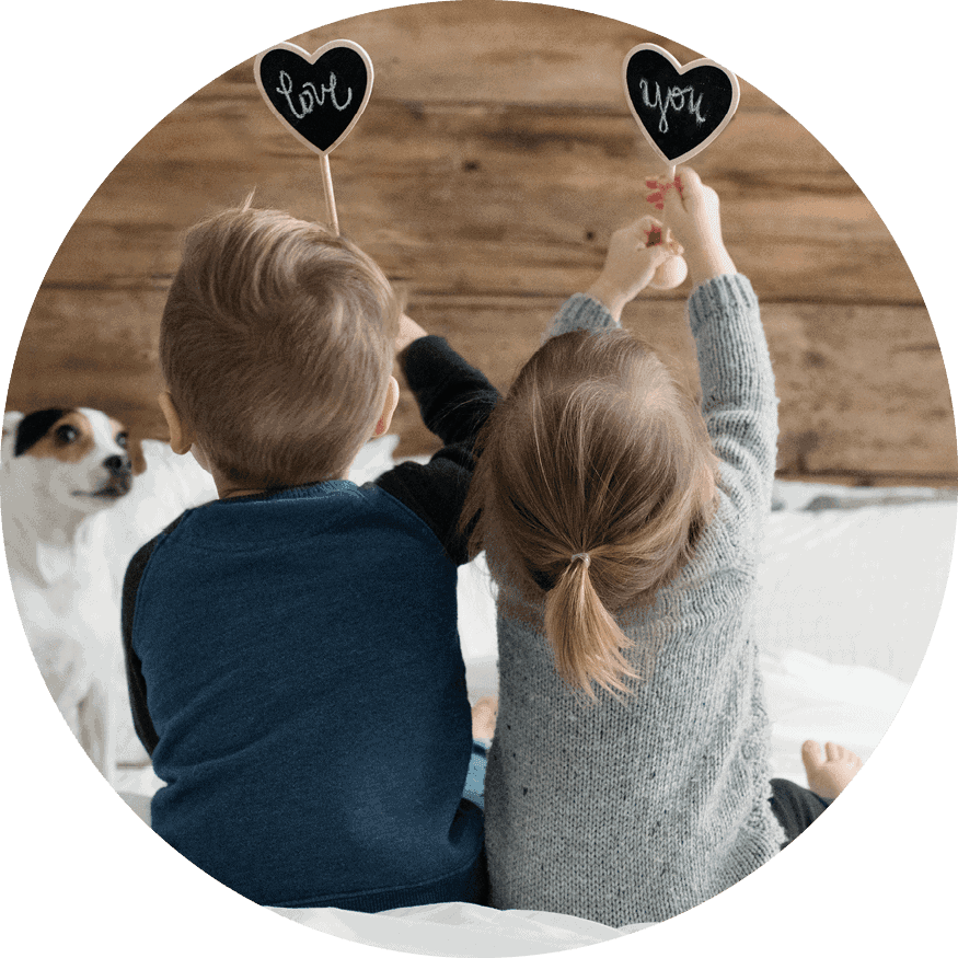 Two children face the wall and hold heart-shaped signs that read "love" and "you."