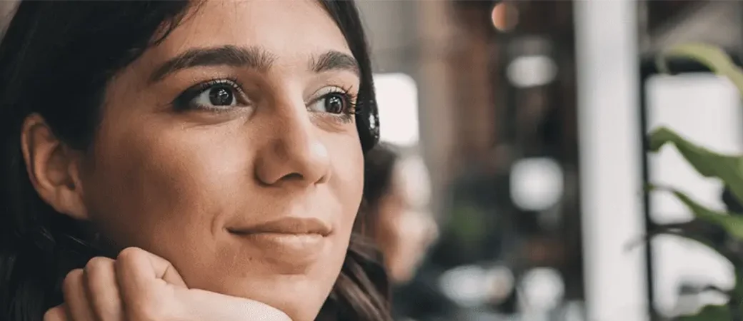 A woman in a light brown leather jacket looks out the window with a hopeful expression.