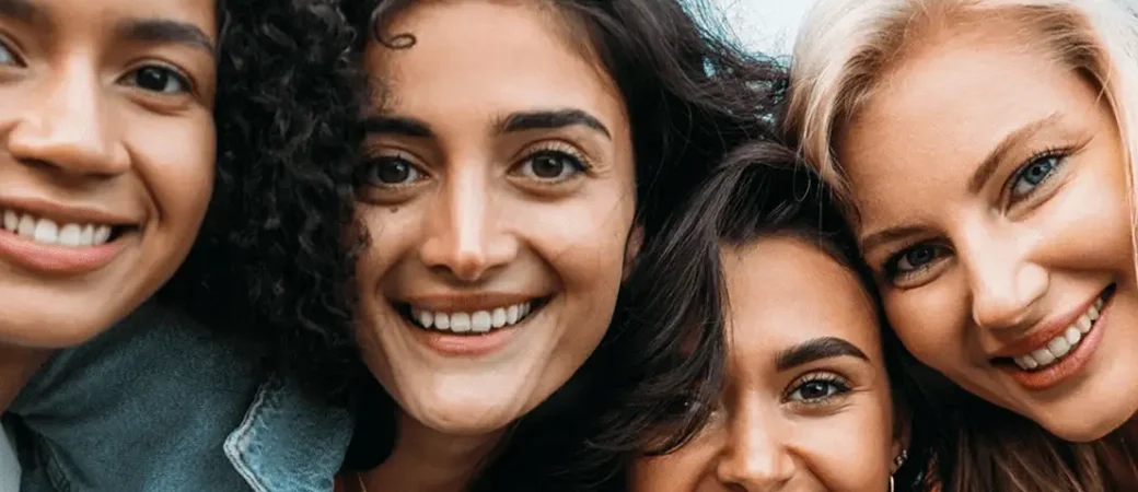 A diverse group of women come in close together and smile.
