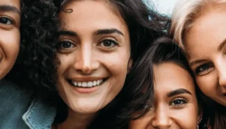 A diverse group of women come in close together and smile.