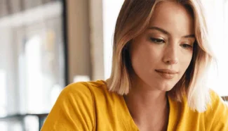 A woman in a yellow t-shirt looks engaged with her computer screen, looking at egg donor disqualifications.