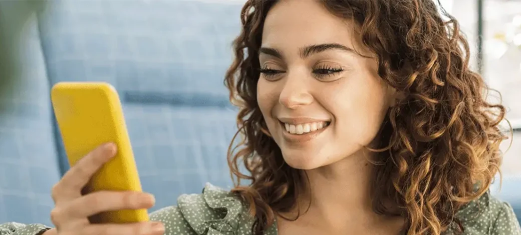 Egg donor smiling at phone as she reads the reasons she should donate eggs.
