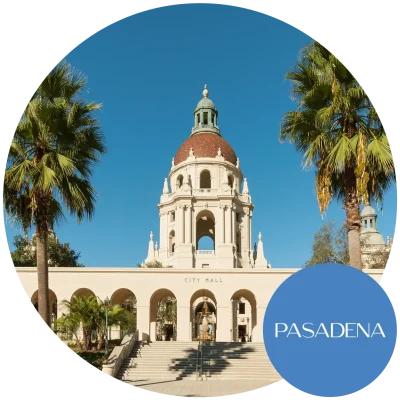 A daytime view of the Pasadena, CA city hall from the front lined with palm trees.